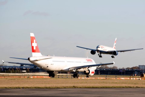 A British Airways jet approaches Heathrow Airport past a Swissair jet on the tarmac in London